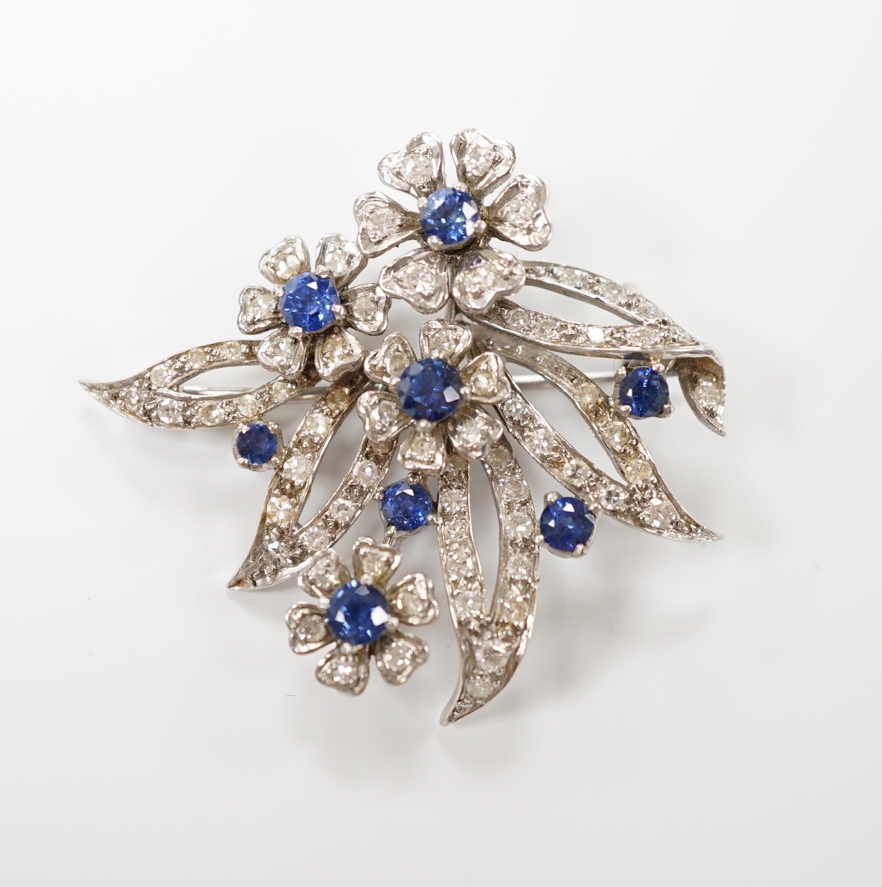 A white metal (stamped 18 plat), sapphire and diamond chip cluster set foliate brooch, 32mm, gross weight 11 grams.